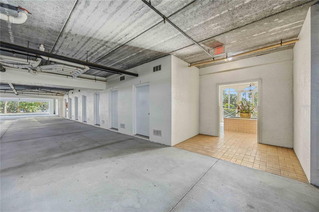 A covered parking area features concrete ceilings, white walls, storage doors, and a tiled entryway — 200 HARBOR WALK DRIVE UNIT 322, PUNTA GORDA, FL