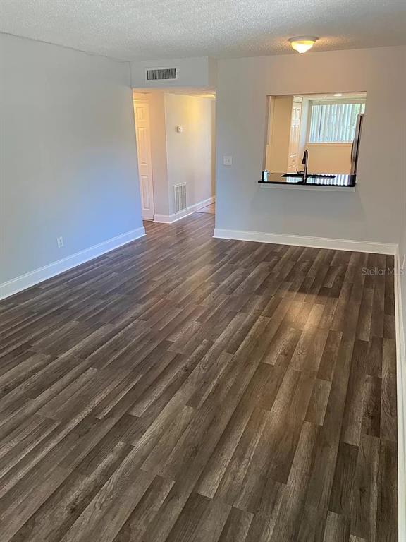 A living room with wood-look flooring, a ceiling light, and a kitchen pass-through window — 6308 NEWTOWN CIRCLE UNIT 8B1, TAMPA, FL