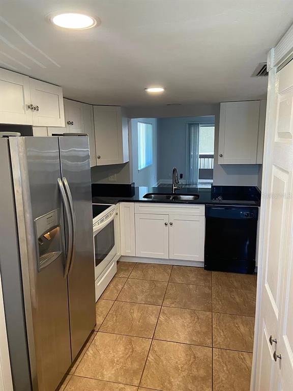 A kitchen with white cabinets, stainless steel refrigerator, black countertops, and tan tile flooring — 6308 NEWTOWN CIRCLE UNIT 8B1, TAMPA, FL