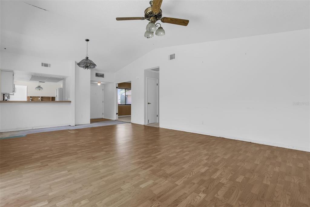 An empty living room with wood-look flooring, a ceiling fan, and a pass-through kitchen window — 361 KANTOR BOULEVARD, CASSELBERRY, FL