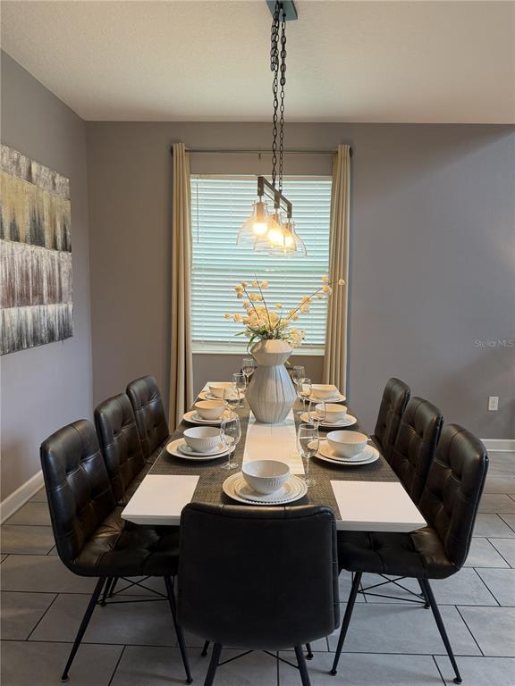 A dining room features a long table with eight black chairs and a central light fixture — 2833 BOOKMARK DRIVE, KISSIMMEE, FL