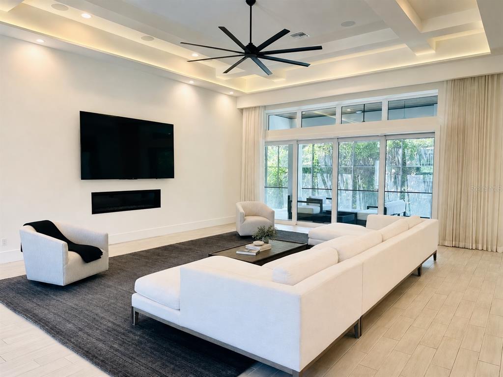 A modern living room features a white sectional, two armchairs, a fireplace, and large glass doors — 5021 W HOMER AVENUE, TAMPA, FL