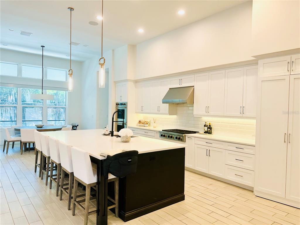 A modern kitchen features a large black island, white cabinetry, and light wood-look tile flooring — 5021 W HOMER AVENUE, TAMPA, FL