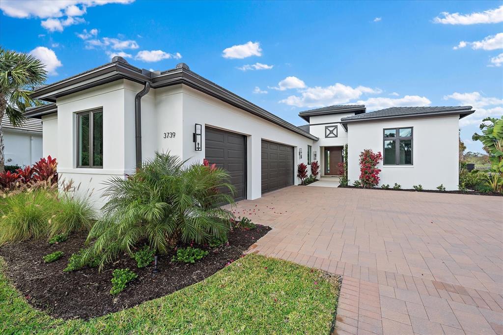 A modern single-story house with a white stucco exterior, dark garage doors, and paved driveway — 3739 CALEDONIA LANE, SARASOTA, FL