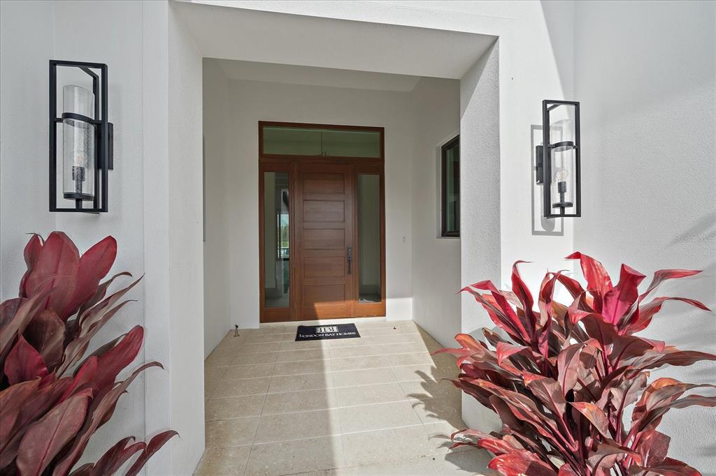 A modern entryway features a wooden front door, tiled flooring, and two black wall sconces — 3739 CALEDONIA LANE, SARASOTA, FL