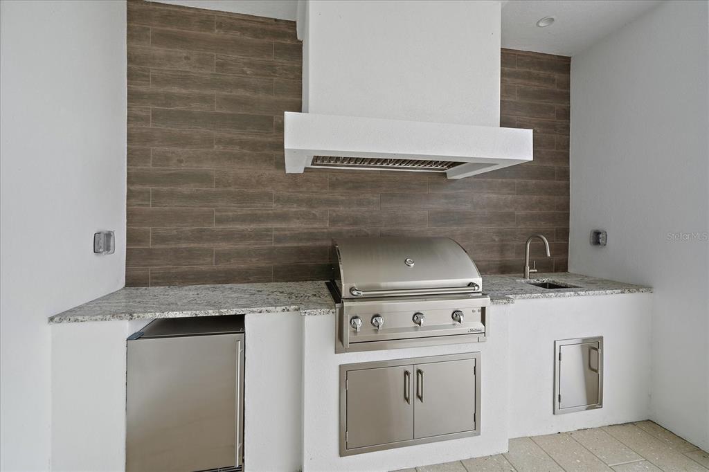 An outdoor kitchen features a stainless steel grill, a sink, and wood-look tile backsplash — 3739 CALEDONIA LANE, SARASOTA, FL