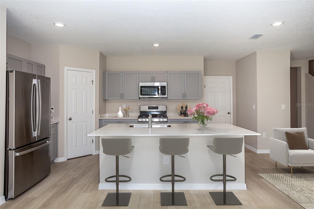 A kitchen features gray cabinets, stainless steel appliances, a white island, and three bar stools — 1743 VANILLA STREET, HAINES CITY, FL