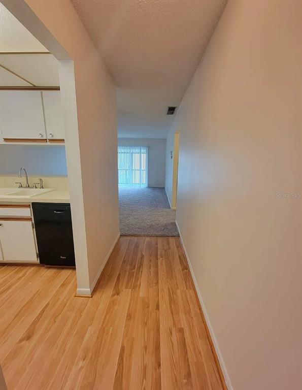 A kitchen with white cabinets and a black dishwasher opens into a carpeted living area — 100 E KENTUCKY AVENUE UNIT 103D, DELAND, FL