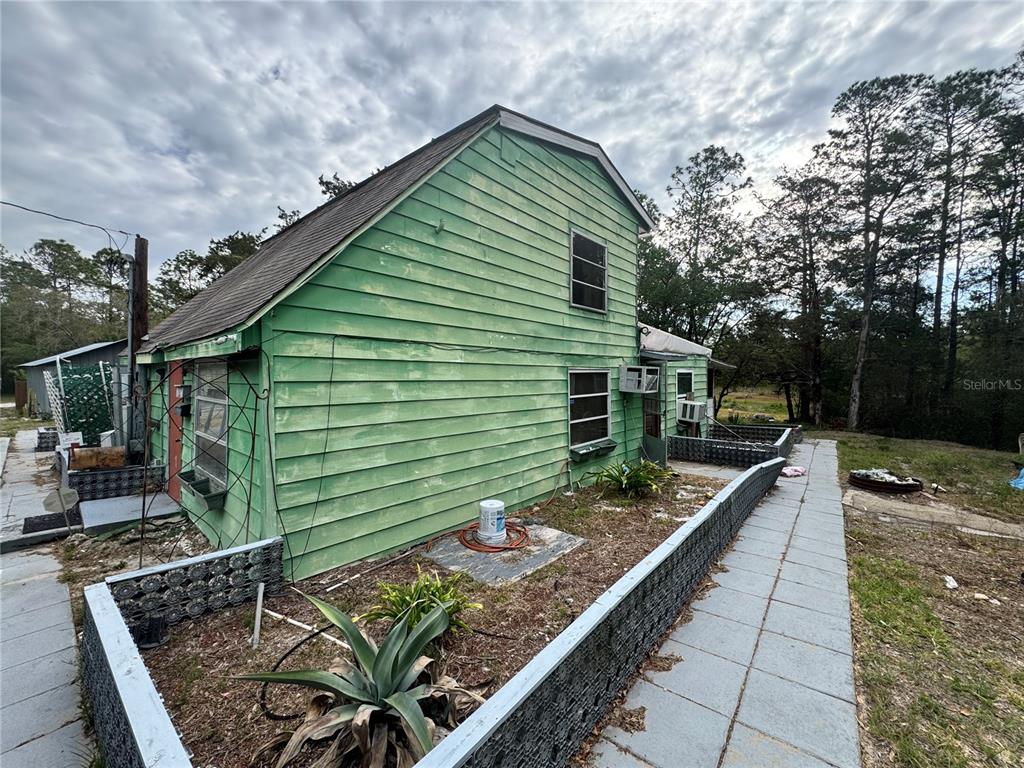 The exterior of a two-story green house features horizontal siding and a raised garden bed — 17528 COYOTE ROAD, HUDSON, FL