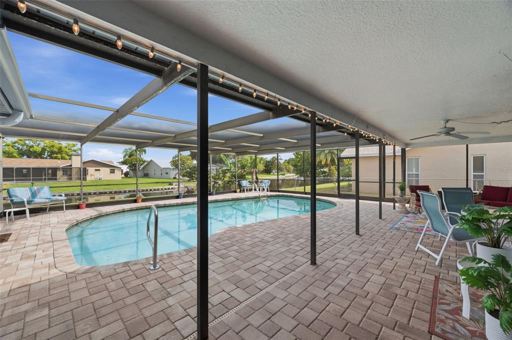 A screened-in patio features a swimming pool, paver flooring, and views of a canal — 10744 97TH STREET, LARGO, FL
