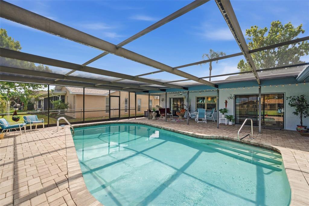 A screened-in swimming pool with a paver deck and patio furniture under a covered lanai — 10744 97TH STREET, LARGO, FL