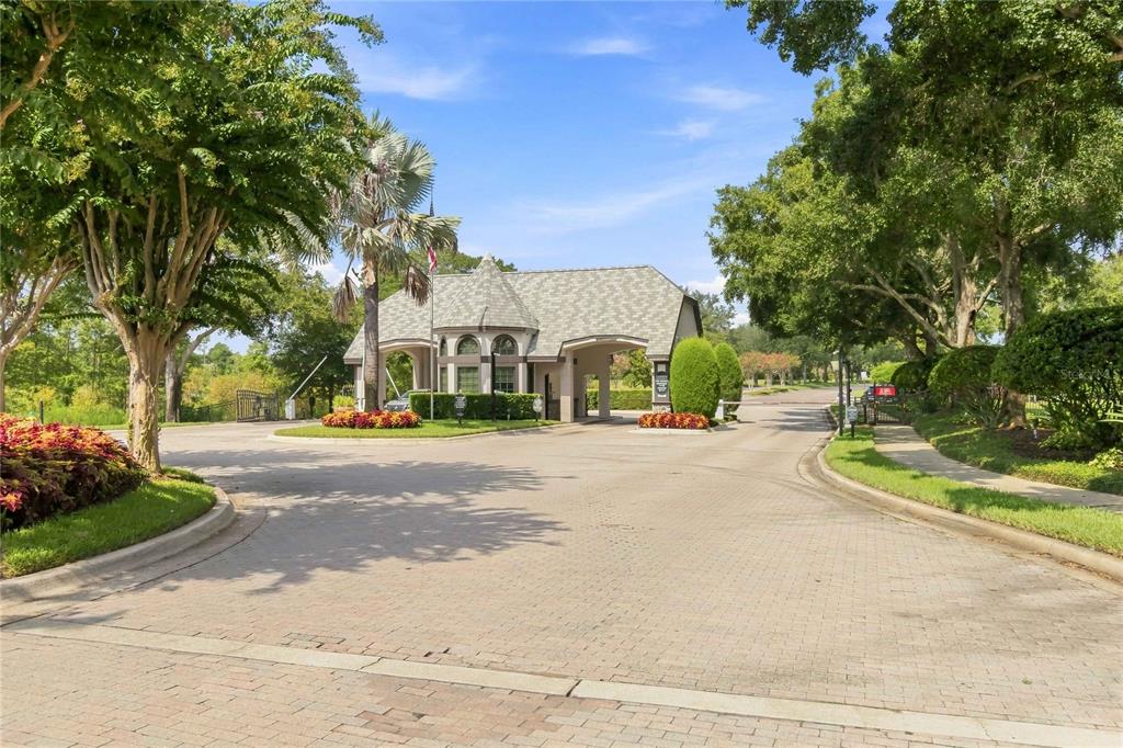 A paved entrance road leads to a gated community guardhouse surrounded by trees and landscaping — 1038 WESTBURY WAY, LAKE MARY, FL