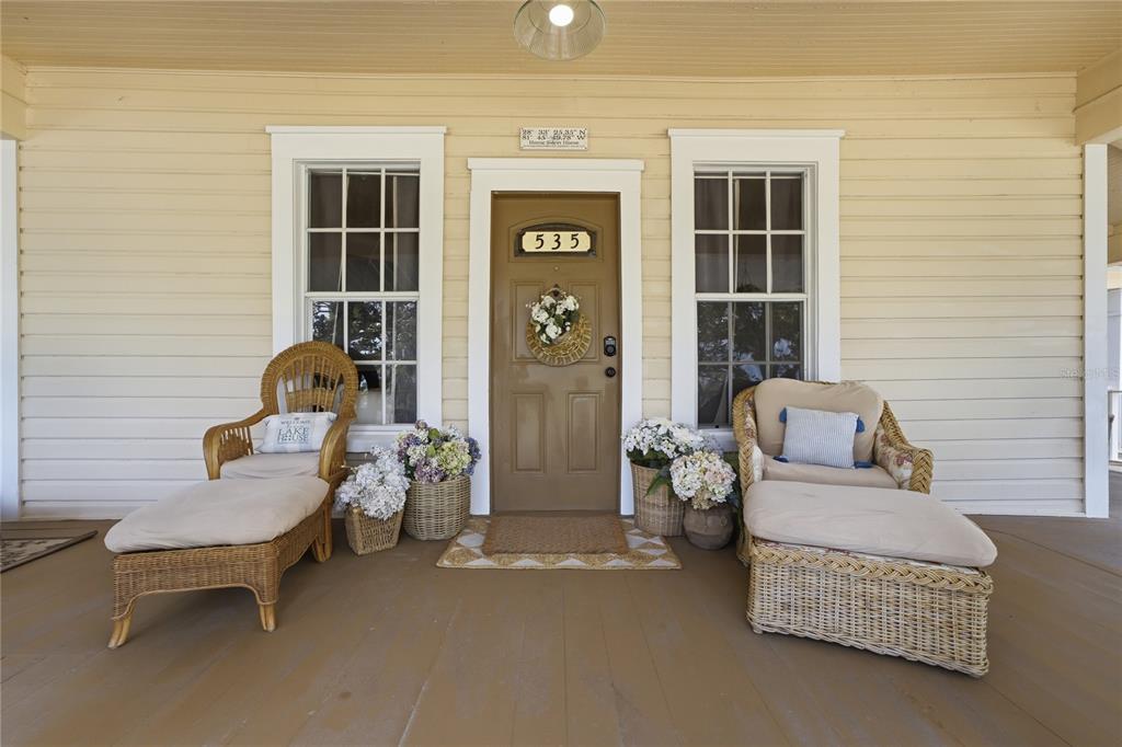 A covered front porch features a brown door, two wicker chairs with ottomans, and flowers — 535 W OSCEOLA STREET, CLERMONT, FL