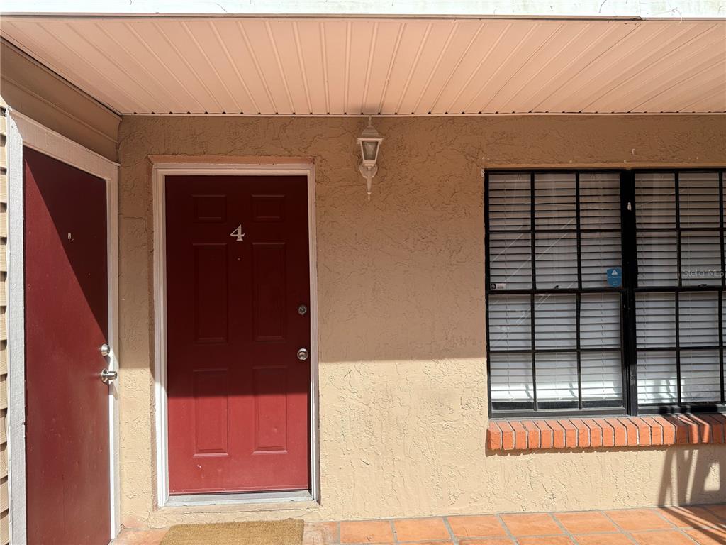 A red front door numbered four sits beside a window with black shutters and blinds — 21038 VOYAGER BOULEVARD UNIT 4, LAND O LAKES, FL
