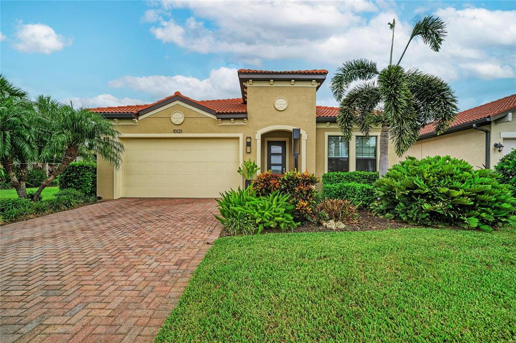 A single-story house with a tan stucco exterior, red tile roof, and a paved driveway — 10121 MARBELLA DRIVE, BRADENTON, FL