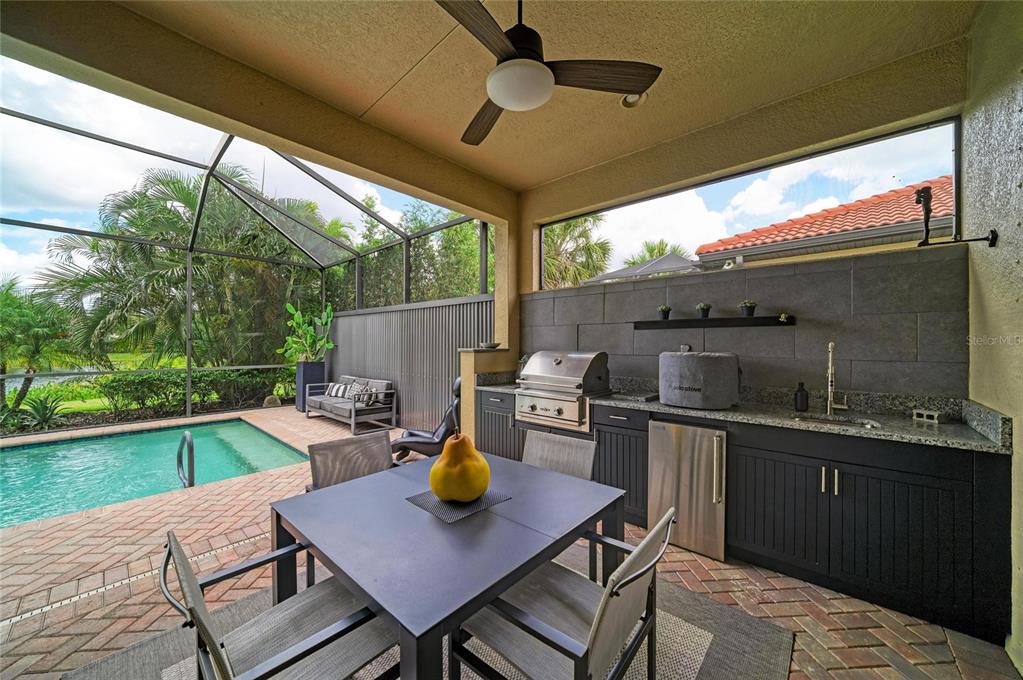 A covered outdoor patio features a dining set, a built-in kitchen, and a swimming pool — 10121 MARBELLA DRIVE, BRADENTON, FL