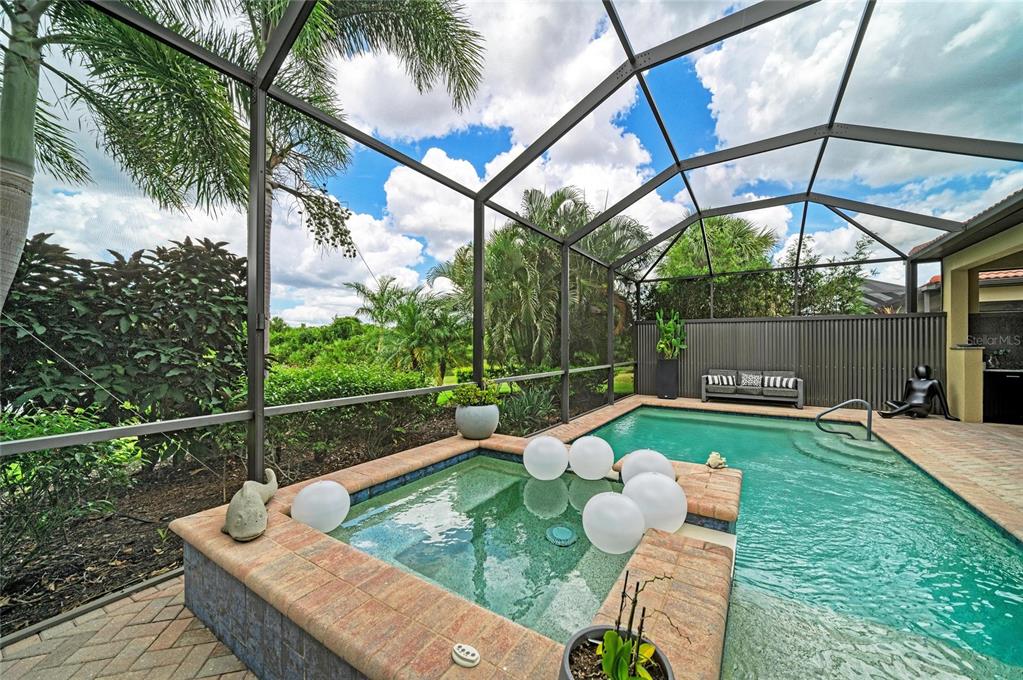 A screened-in pool and hot tub area with brick coping and tropical landscaping — 10121 MARBELLA DRIVE, BRADENTON, FL