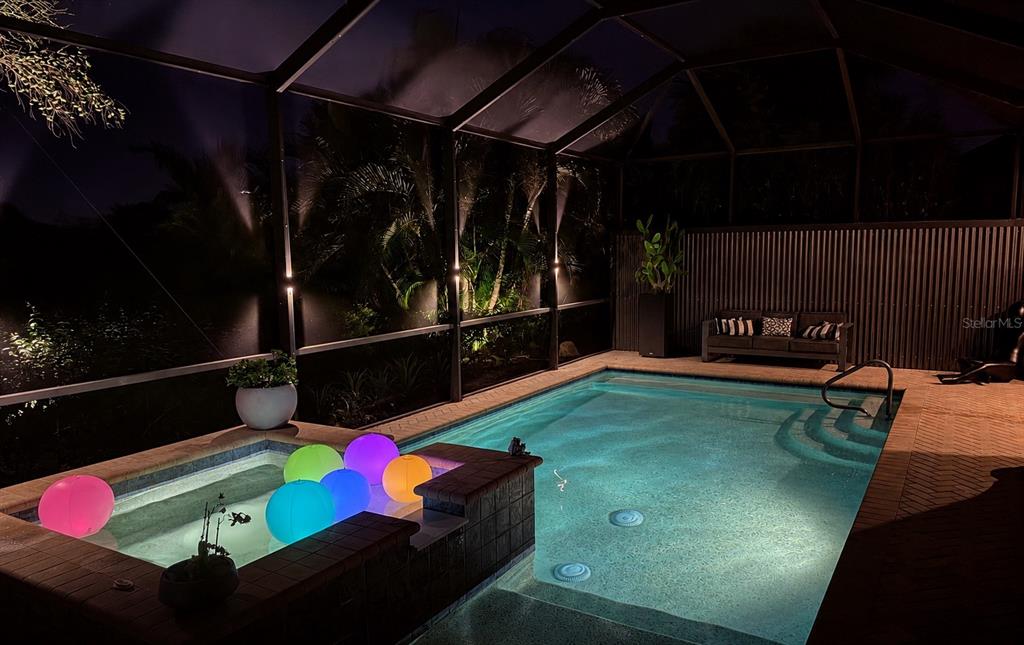 A screened-in pool and spa area at night with glowing floating balls — 10121 MARBELLA DRIVE, BRADENTON, FL