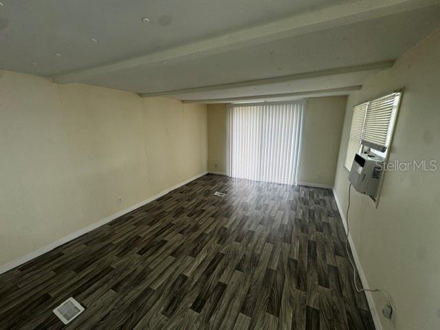 An empty room features wood-look laminate flooring, white walls, a sliding glass door, and windows — 7130 COMMONS BOULEVARD, PORT RICHEY, FL