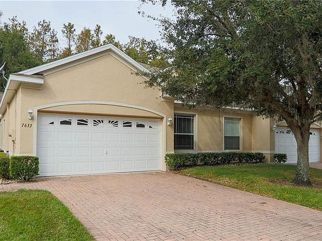 A single-story house with a beige stucco exterior, a two-car garage, and a brick driveway — 7633 WIMPOLE DRIVE, NEW PORT RICHEY, FL