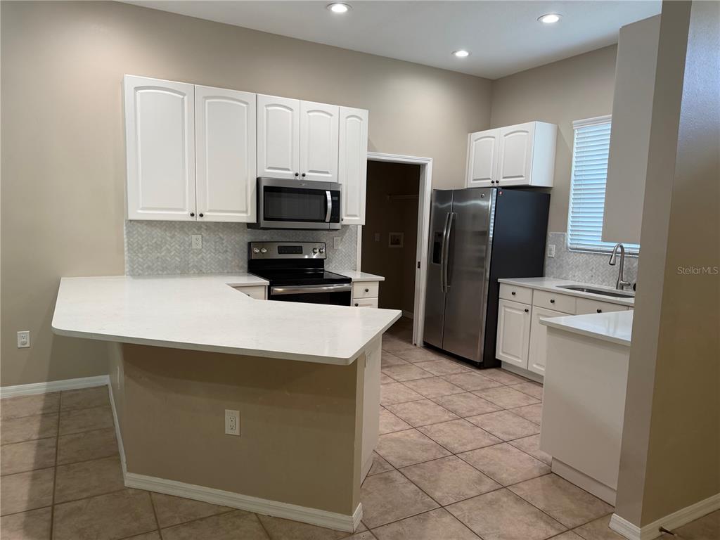 A kitchen features white cabinets, stainless steel appliances, a peninsula, and light-colored countertops — 7633 WIMPOLE DRIVE, NEW PORT RICHEY, FL