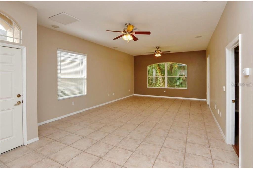 An empty room with beige tile floors, two ceiling fans, and a large arched window — 7633 WIMPOLE DRIVE, NEW PORT RICHEY, FL