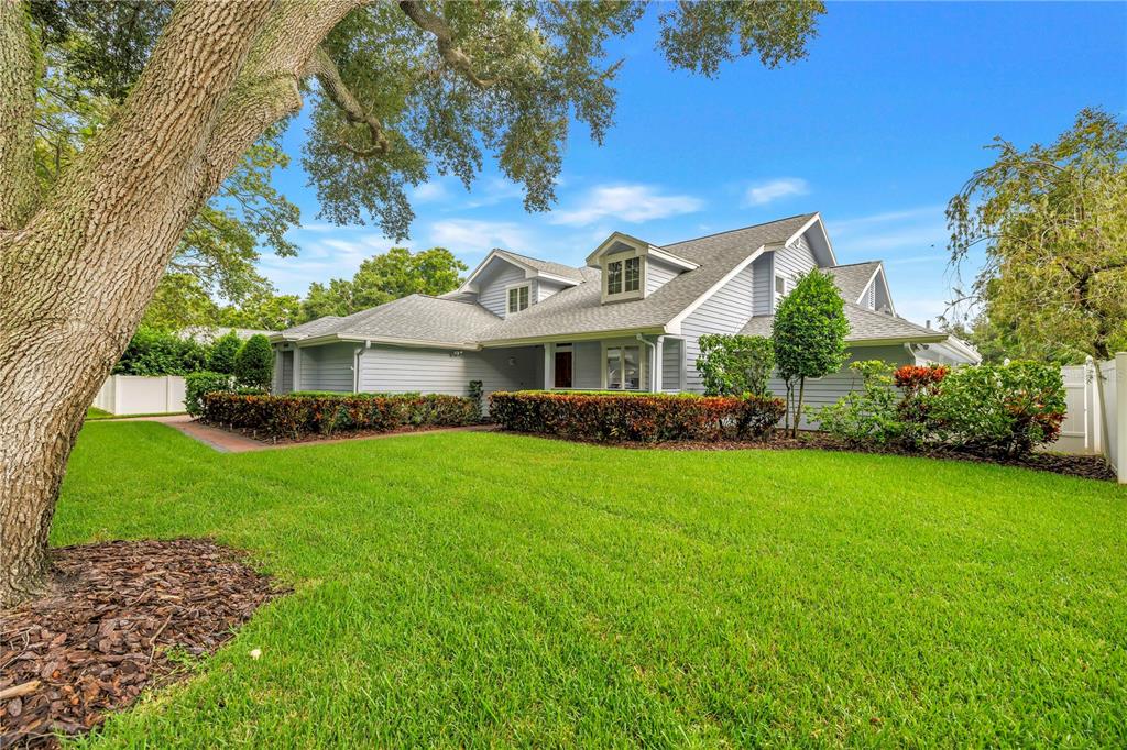 A light blue house with a gray roof and dormer windows sits behind a green lawn — 12383 WINDTREE BOULEVARD, SEMINOLE, FL