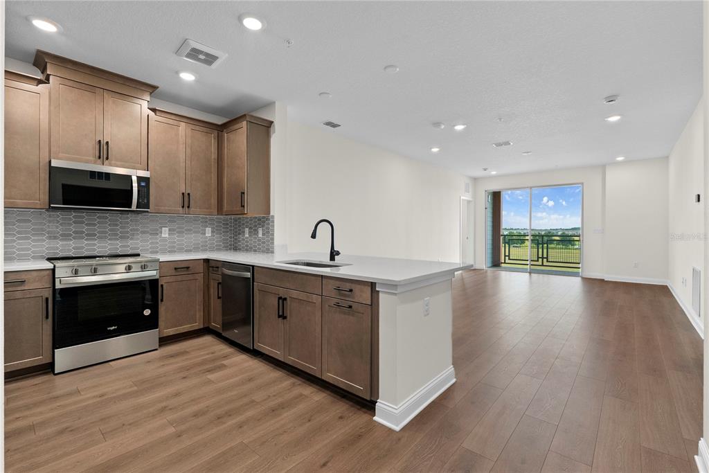 A modern kitchen with wood cabinets and stainless steel appliances opens to a living area — 7545 LAUREATE BOULEVARD UNIT 7404, ORLANDO, FL