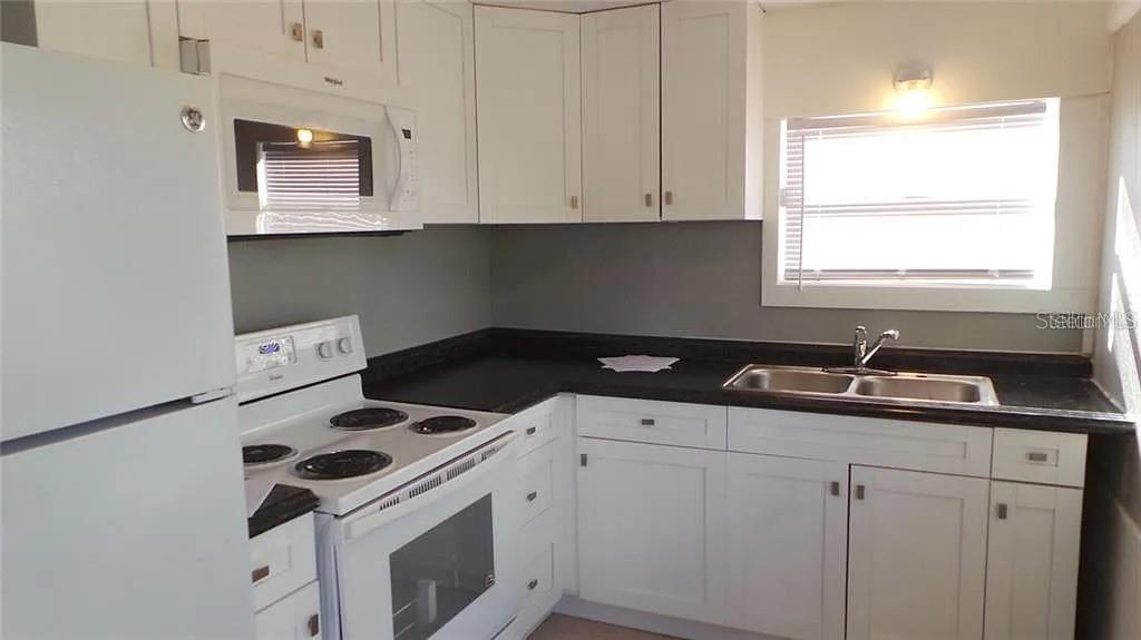 A kitchen with white cabinets, black countertops, a white stove, and a stainless steel sink — 707 AVENUE B SW UNIT B, WINTER HAVEN, FL