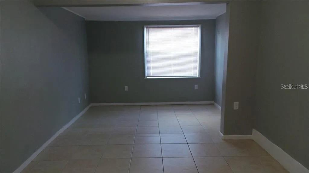 An empty room features gray walls, light-colored tile flooring, and a single window with blinds — 707 AVENUE B SW UNIT B, WINTER HAVEN, FL