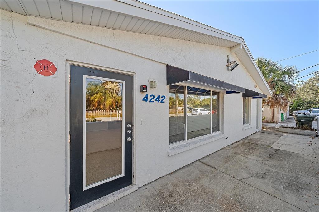 The exterior of a white stucco building features a black-framed glass door and windows — 4242 MCINTOSH LANE, SARASOTA, FL