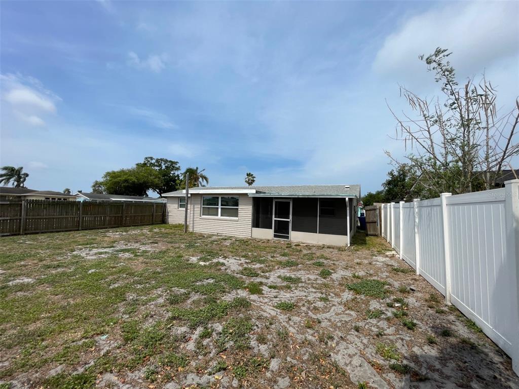 A backyard view of a single-story house with a screened-in porch and white vinyl fencing — 2702 DRUID PLACE, HOLIDAY, FL