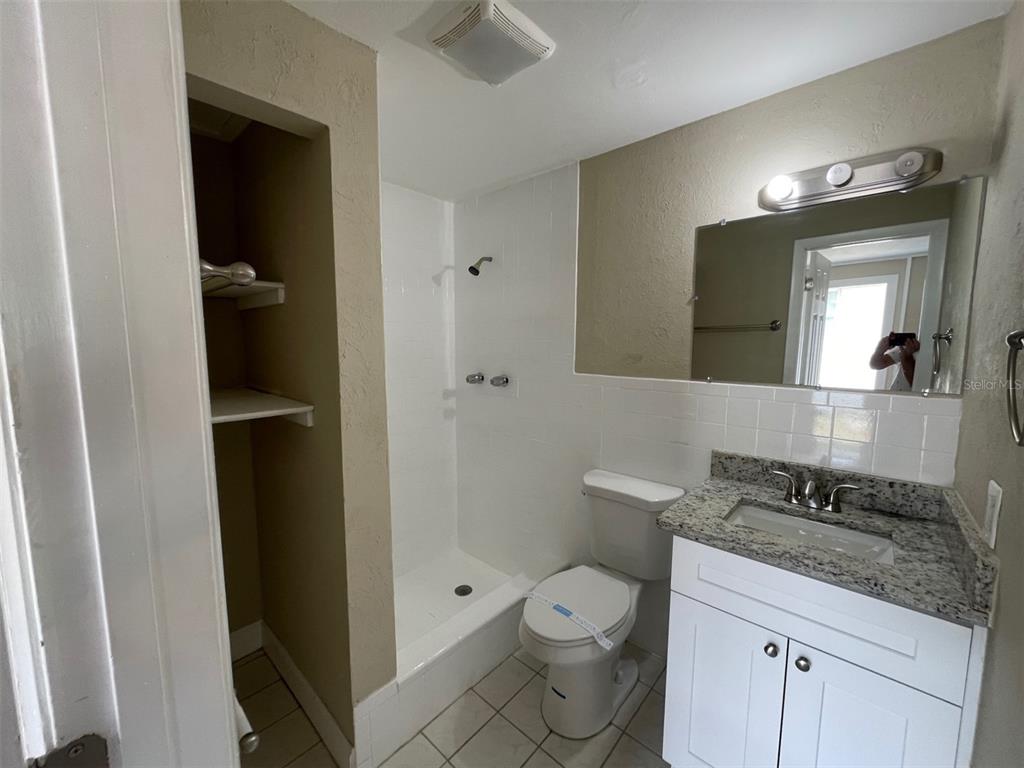 A bathroom features a walk-in shower, a white vanity with granite countertop, and a toilet — 2702 DRUID PLACE, HOLIDAY, FL