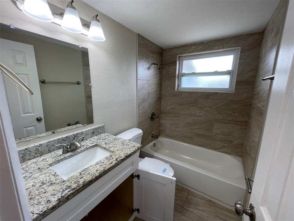 A bathroom features a granite vanity, a white cabinet, and a tiled tub-shower combination — 2702 DRUID PLACE, HOLIDAY, FL