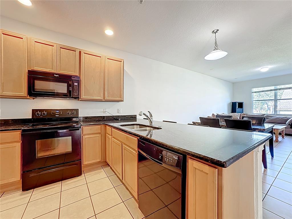 A kitchen features light wood cabinets, black appliances, dark countertops, and tile flooring — 1991 SWITCH GRASS CIRCLE, OCOEE, FL