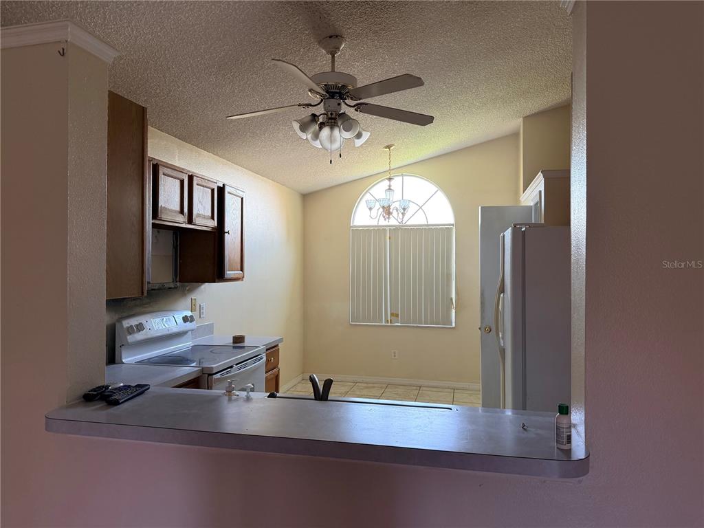 A kitchen with wood cabinets, white appliances, and a breakfast bar overlooking a dining area — 863 COUNTRY CROSSING COURT, KISSIMMEE, FL