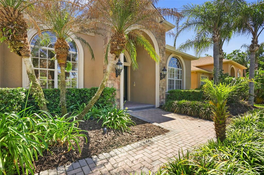 A stone-accented house entrance features an arched doorway, a brick walkway, and palm trees — 27608 PINE POINT DRIVE, WESLEY CHAPEL, FL