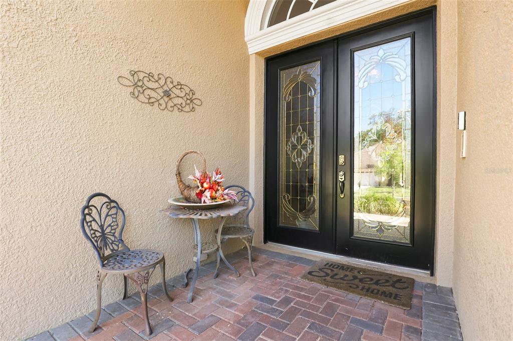 A front entryway features double glass-paneled doors, a brick patio, and a small bistro set — 27608 PINE POINT DRIVE, WESLEY CHAPEL, FL
