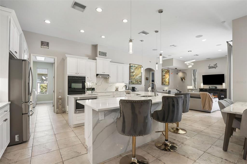 A modern kitchen features white cabinetry, a marble-topped island with bar stools, and tile flooring — 27608 PINE POINT DRIVE, WESLEY CHAPEL, FL