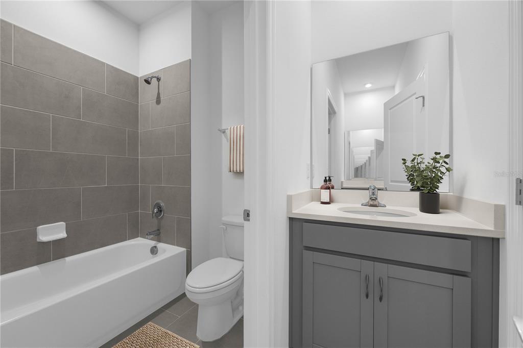 A bathroom features a gray vanity, a white toilet, and a tub with gray tile walls — 6743 WINTERBERRY DRIVE, LAKE HAMILTON, FL