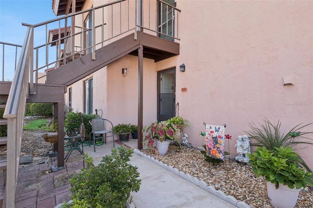 The exterior of a peach-colored building features a concrete walkway, potted plants, and wooden stairs — 121 LA CASA UNIT 121, LAKE WALES, FL
