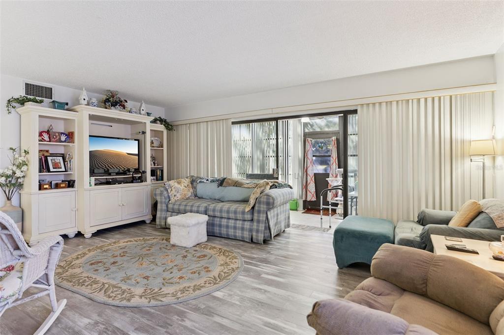 A living room features a plaid sofa, a white entertainment center, and sliding glass doors — 121 LA CASA UNIT 121, LAKE WALES, FL