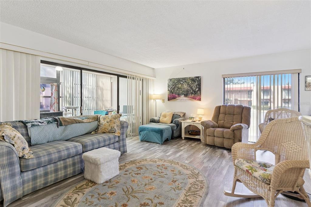 A living room features wood-look flooring, a plaid sofa, a recliner, and a wicker chair — 121 LA CASA UNIT 121, LAKE WALES, FL