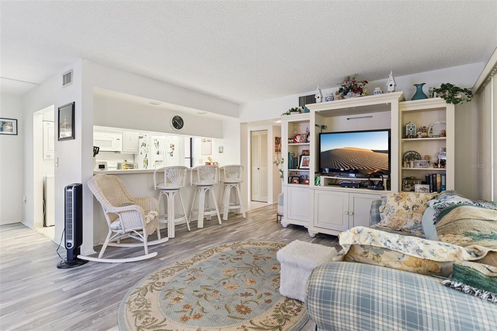 A living room with light wood-look flooring, a white entertainment center, and a breakfast bar — 121 LA CASA UNIT 121, LAKE WALES, FL