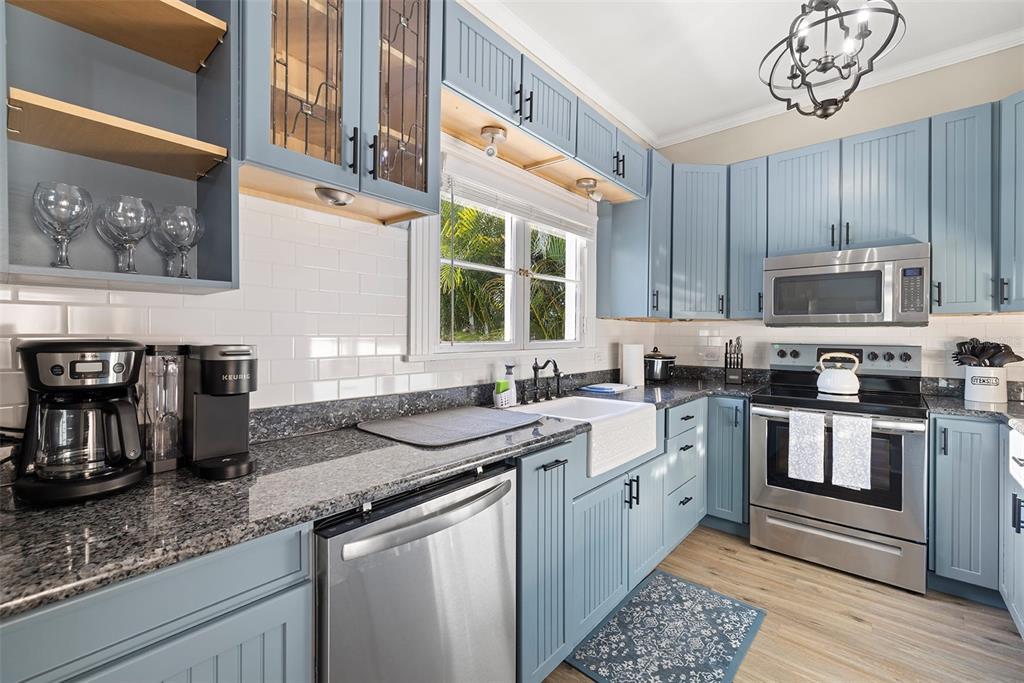 A kitchen features blue beadboard cabinets, granite countertops, stainless steel appliances, and a farmhouse sink — 551 OMAHA STREET, PALM HARBOR, FL
