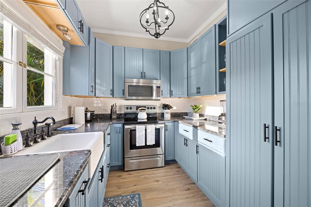 A kitchen features light blue beadboard cabinets, dark granite countertops, and a white farmhouse sink — 551 OMAHA STREET, PALM HARBOR, FL