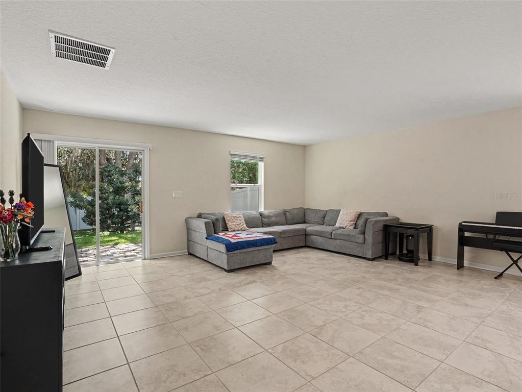 A living room features light tile flooring, a large gray sectional sofa, and sliding glass doors — 4469 BLUFF OAK LOOP, KISSIMMEE, FL