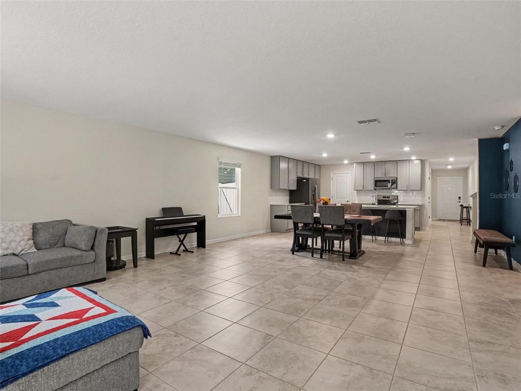 An open-concept living and dining area features tile flooring, grey cabinetry, and a kitchen island — 4469 BLUFF OAK LOOP, KISSIMMEE, FL
