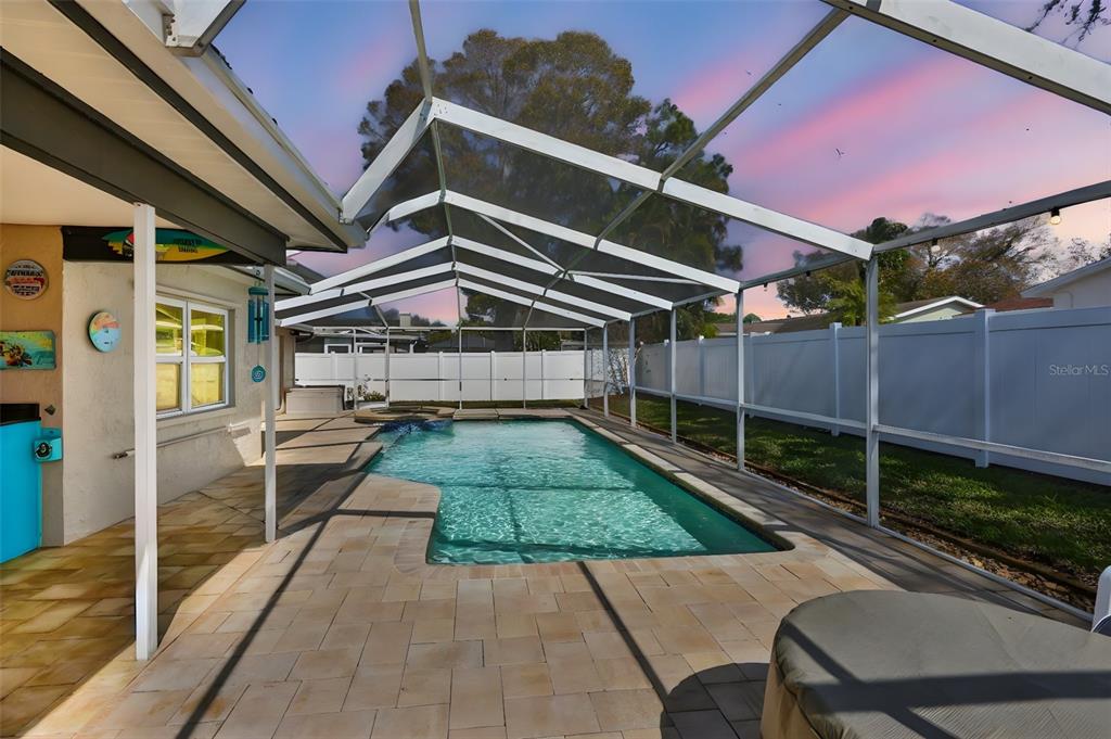 A screened-in swimming pool with a paver patio sits in a fenced backyard at sunset — 9275 133RD STREET, SEMINOLE, FL