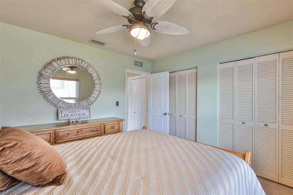 A bedroom features a bed, a dresser with a round mirror, and white louvered closet doors — 9275 133RD STREET, SEMINOLE, FL